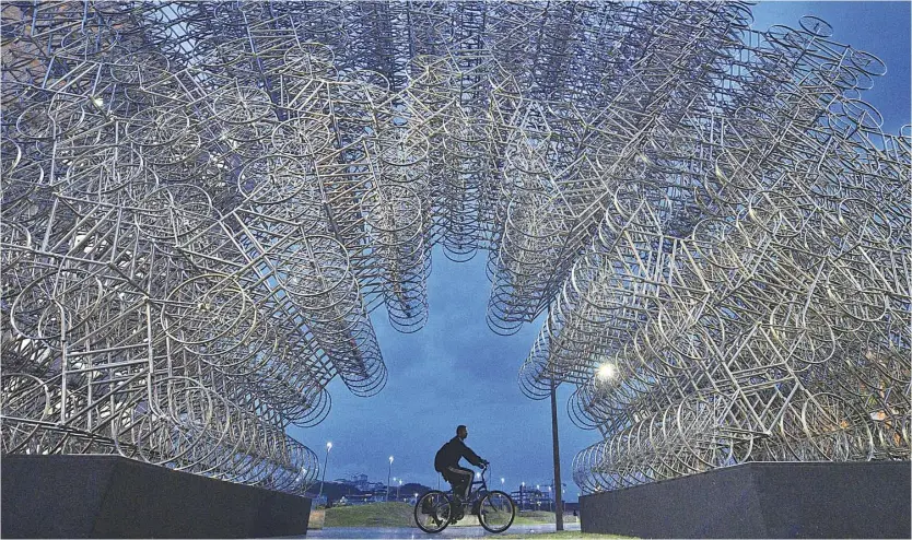  ?? AFP ?? Forever cycles A man rides his bike past an art installati­on by Chinese artist Ai Weiwei in Rio de Janeiro, Brazil. The design is comprised of over 1,000 stainless steel bicycles.