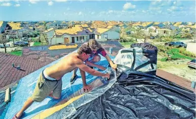  ??  ?? Tom Mastandrea, 16, and Nathan Watarz, 22, patch up Mastandrea’s roof in Kendall the day after Andrew hit.