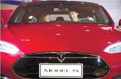  ?? (AP PHOTO) ?? TEST DRIVE. In this photo taken in April,two men check out the interiors of a Tesla Model S electric car on display at the Beijing Internatio­nal Automotive Exhibition. Tesla Motors shipped fewer cars in the past three months and is unlikely to meet its...