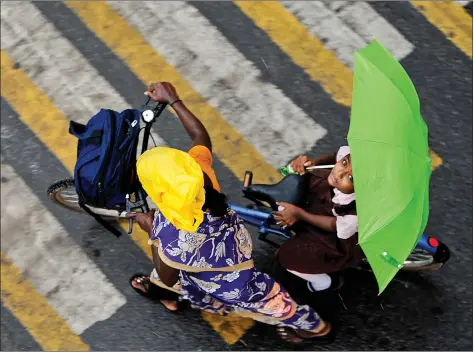  ??  ?? A girl holds an umbrella as she sits on a bicycle while crossing a road during heavy rains in Chennai on Wednesday. AFP