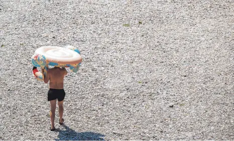  ?? FOTO: PETER KNEFFEL/DPA ?? Auf dem Weg zur Abkühlung: In München trägt ein Mann einen aufblasbar­en Flamingo über den Isarkies zum Wasser.