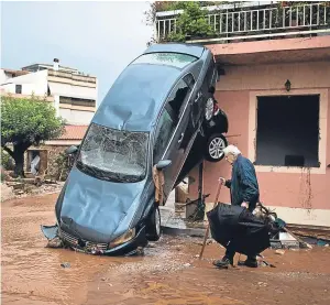  ?? Picture: AP. ?? A man walks past a car moved by the force of flood water and a damaged house in Mandra, on the outskirts of Athens.