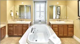  ??  ?? The master bathroom offers his-and-hers marble vanities, jetted soaking tub with marble tile surround and travertine floors.