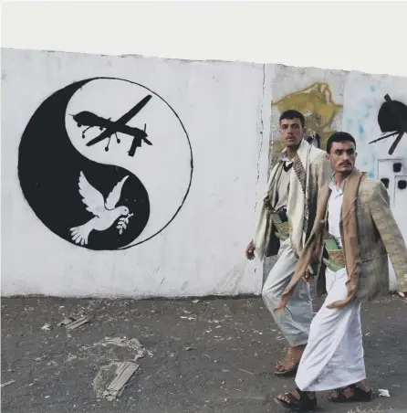  ?? PICTURE: AFP/GETTY IMAGES ?? 0 Yemeni men walk past a mural depicting a US drone and a dove in a yin-yang symbol