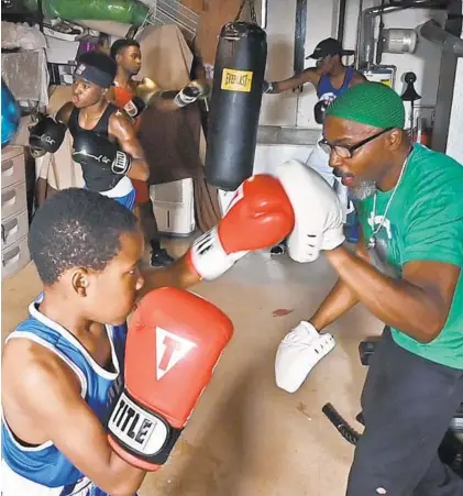  ?? KENNETH K. LAM/BALTIMORE SUN ?? Shawn Robinson, right, trains with his youngest son Yusuf, 10, in the family’s basement gym while in the background his other sons do workouts on bags. Robinson is preparing his four sons for a national boxing tournament this month.