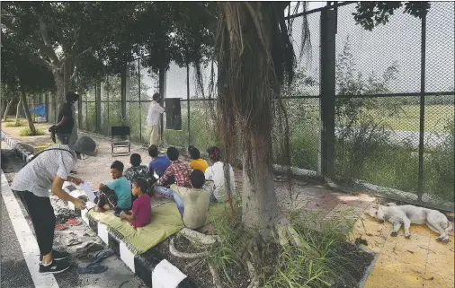  ??  ?? A stray dog sleeps on a sidewalk as former diplomat Virendra Gupta (far right) and his singer wife Veena Gupta teach underprivi­leged children in New Delhi on Sept. 3. The Indian couple hold free classes for underprivi­leged children on a sidewalk in New Delhi with the goal to keep them learning and not left behind when schools open. As most schools in India remain shut since late March when the country imposed a nationwide lockdown to curb the spread of covid-19, many switched to digital learning and taking classes online.
(AP/Manish Swarup)