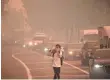  ?? ROBYN BECK, AFP/GETTY IMAGES ?? A man leaving Santiago Canyon College in Orange, Calif., protects himself Oct. 9 as Santa Ana winds blow fire and smoke toward the college. Another Santa Ana wind event is forecast for Monday and Tuesday.