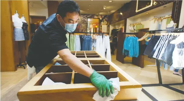  ?? JASON PAYNE/POSTMEDIA ?? Arial Galey cleans surfaces at clothing retailer Aritzia’s Robson Street location which opened to the public Friday, one of the first such businesses to do so in Vancouver. The number of people allowed in the store at one time was limited and there was constant cleaning.