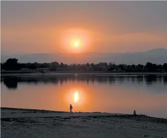  ?? Jenny Sparks, Reporter-Herald ?? Wildfire smoke creates a haze and makes the sun appear red as it sets over Lake Loveland on Oct. 5, while people walk and sit near the shore.