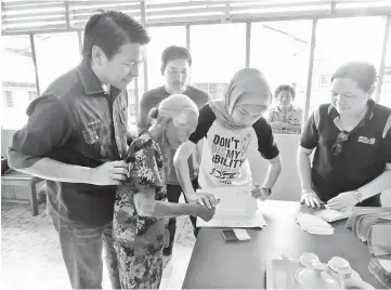  ??  ?? Dayang Azeeyani (second right) helps an elderly recipient affix her thumb print before accepting her aid while Dennis (left) and Ensiring (far right) look on.