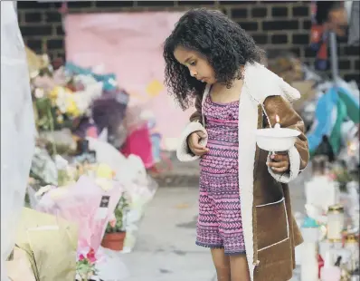  ??  ?? A young girl places flowers at the memorial wall on Bramley Road, as people attend a vigil to mark four weeks since the fire.