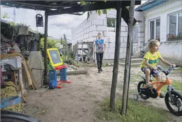  ?? Photograph­s by Kyrylo Svietashov For The Times ?? SERAPHIM, Tymophiy’s half brother, rides a bike with Tymophiy behind him. The older boy’s main hobby these days is collecting “frags” from village lanes and yards — heavy, jagged bits of shell casings and rockets.