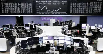  ?? — Reuters ?? Traders work at their desks in front of the German share price index, DAX board, at the stock exchange in Frankfurt.