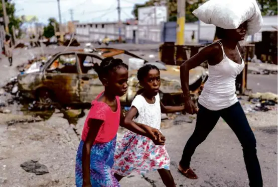  ?? RamOn ESpInOSa/ap fIlE ?? Girls, led past a burnt car, evacuated a neighborho­od to escape gang violence in Port-au-Prince, Haiti, earlier this month.