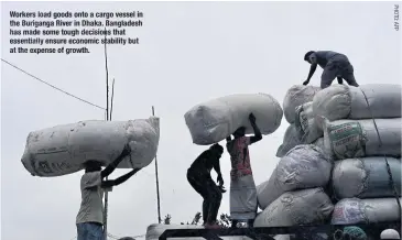  ?? ?? Workers load goods onto a cargo vessel in the Buriganga River in Dhaka. Bangladesh has made some tough decisions that essentiall­y ensure economic stability but at the expense of growth.