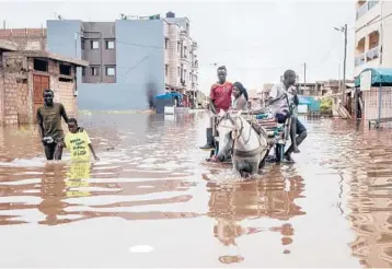  ?? JOHN WESSELS/GETTY-AFP ?? Senegal flooding: People make their way through the flooded neighborho­od of Keur Massar in Dakar, Senegal, on Friday. Each year the neighborho­od of Keur Massar deals with heavy flooding during the peak of the rainy season. Families living in Keur Massar pack up their belongings and move out of the area during this period.