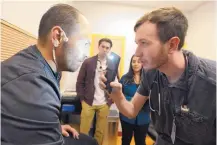  ??  ?? Samuel MacDonald, right, a first-year medical student at the University of New Mexico, uses the light from his phone as he examines Jesse James Kershner, a homeless man, at AOC. On Tuesday evenings, students from UNM’s Health Sciences Center volunteer...