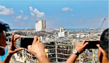  ?? — AFP ?? People take photos from atop a bridge overlookin­g the damaged port of Lebanon’s capital Beirut and its grain silos on Sunday, in the aftermath of a colossal explosion that occurred Tuesday due to a huge pile of ammonium nitrate that had languished for years at a port warehouse.