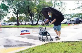  ?? Lynne Sladky / Associated Press ?? Franklin Castellon, 76, shields himself from the rain as he walks to an early voting site on Monday in Miami. Florida begins in-person early voting Monday in much of the state as the Trump campaign tries to cut into an early advantage Democrats have posted in mail-in votes in the key swing state.