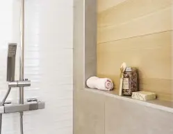  ??  ?? L'espace douche rappelle les matériaux qui habillent la salle de bain, soit la céramique grise et celle en relief. La niche taillée dans le mur se distingue par ses carreaux imitant l'aspect de planches de bois.
