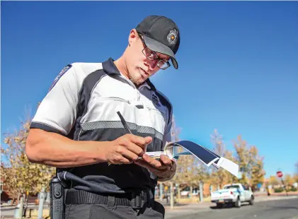  ??  ?? Parking enforcemen­t officer Brandon May writes a ticket by hand for a vehicle not displaying a receipt for parking Monday near the Santa Fe Railyard. Officers have been writing parking tickets by hand since last Friday and will continue until they...