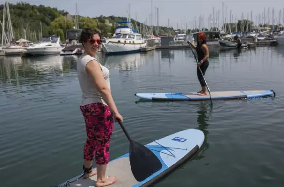  ?? ALLEN AGOSTINO/TORONTO STAR ?? Paddleboar­ders Lisa Didomizio, front, and Nadine Dahdah make their way through the float homes community. For more on lakeside living in the city,