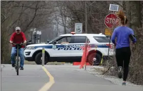  ?? (AP/Michael Conroy) ?? Police block a section of a trail in Carmel, Ind., on Thursday. In big cities and remote areas alike, officers are being told to issue tickets or summons rather than making arrests for minor crimes as law enforcemen­t agencies try to limit exposure to the coronaviru­s.