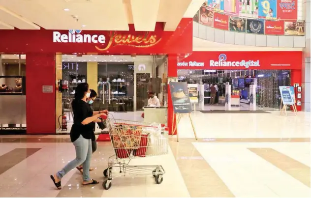  ?? Reuters ?? ↑
A customer pushes a trolley with grocery items past Reliance Jewels and Reliance Digital stores in Mumbai, India.