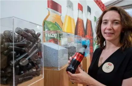  ?? FOTO JORIS HERREGODS ?? An Vermeulen, directeur van Coca-Cola in België, toont een flesje cola dat van gerecyclee­rd materiaal is gemaakt. In de bak links vooraan liggen de preforms, de gerecyclee­rde basis voor de nieuwe flesjes.