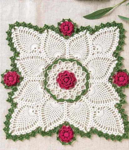  ??  ?? This stunning thread doily features pristine white pineapples that form the unusual square design. Accented with a border of dimensiona­l roses, this showstoppe­r brings crochet motifs and pineapples together in perfect style.