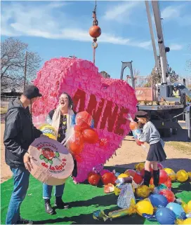  ?? JIM THOMPSON/JOURNAL ?? Anne Bolger-Witherspoo­n picks up some of the giant candy that spilled out of a massive heart piñata made by her husband, Lonnie Anderson, left, and daughter Cheyenne, 11.