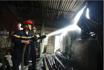 ?? — AFP photo ?? A firefighte­r uses a hose to douse a spot while battling a fire in a workshop complex in Hanoi.