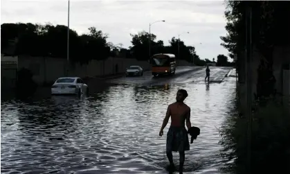  ?? ?? A person walks through floodwater­s near a stranded car along a flooded street in Las Vegas. Photograph: John Locher/AP