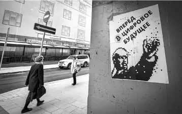  ??  ?? Women walk past a poster bearing an image of the founder of the Soviet Union Vladimir Lenin and a Bitcoin (virtual currency) sign and reading ‘Go forward into the digital future’, downtown Moscow. — AFP photo