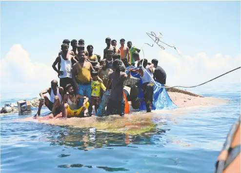  ?? REZA SAIFULLAH / THE ASSOCIATED PRESS ?? Rohingya refugees stand on their capsized boat off the coast of Indonesia on Thursday as rescuers throw them a rope.