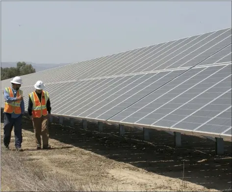  ?? PHOTO/RICH PEDRONCELL­I ?? In this Aug. 17 file photo, solar tech Joshua Valdez (left) and senior plant manager Tim Wisdom walk past solar panels at a Pacific Gas and Electric Solar Plant, in Dixon. AP