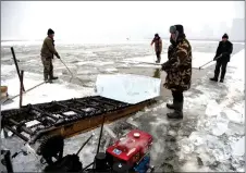  ??  ?? Workers using a machine to cut ice blocks.
Workers guiding an ice block onto a conveyor belt on the frozen Songhua river.
Workers using a conveyor belt to transport a cut ice block.