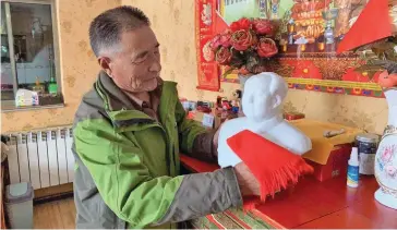  ?? Photo: Xinhua ?? Wang Jianguo wipes the Mao bust at home.