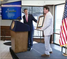  ?? MIKE GROLL/OFFICE OF GOVERNOR ANDREW M. CUOMO ?? Gov. Andrew Cuomo presents Marylou Whitney’s husband, John Hendrickso­n, with a plaque that declares August 3as “Marylou Whitney Day in New York.”