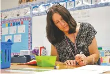  ?? STAFF PHOTO BY C.B. SCHMELTER ?? First-grade teacher Carol Lombardi writes down her students’ lunch numbers while preparing for the first day of school at Hixson Elementary on Tuesday.