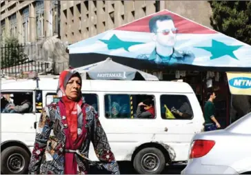  ?? LOUAI BESHARA/AFP ?? A Syrian woman walks past a portrait of President Bashar al-Assad in Damascus on April 7.