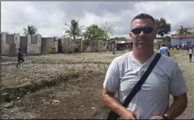  ??  ?? Lance Wilson stands in the town square of Munoz, a village outside of Puerto Plata in the Dominican Republic. This village was ravaged by fire, destroying 64 homes. In the background, the bare earth that used to be the location of many of the destroyed...