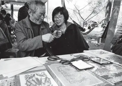  ??  ?? Cai Defu (left), a Shanghai-style paper-cutting master, shows the art of paper cutting to a visitor in Luodian Town in Baoshan District yesterday. — Jiang Xiaowei