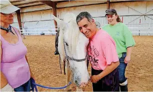  ?? [PHOTOS BY CARLA HINTON, THE OKLAHOMAN] ?? Volunteer leader Tammy Madden watches as camper Tony E. hugs Belle the horse during an equine therapy session at the National Institute on Developmen­tal Delays at St. Gregory’s University in Shawnee. Camp counselor Kelsea McElfresh, at right, looks on.