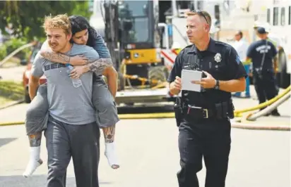  ?? Photos by RJ Sangosti, The Denver Post ?? A man carries a woman who was injured in a natural gas explosion near West Fourth Avenue and Santa Fe Drive in Denver’s Baker neighborho­od Tuesday. A Denver Fire Department spokesman said the gas explosion was the biggest he has seen in about 15 years, when a similar situation happened only blocks away.