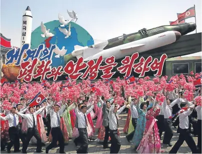  ??  ?? Left: people wave flags and plastic flowers as they walk beside a float with model missiles and words that read “For Peace and Stability in the World” during a military parade in Pyongyang on Saturday. Right: a man watches a TV showing footage of the...