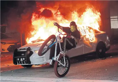  ?? WILFREDO LEE THE ASSOCIATED PRESS ?? A protester rides past a burning police car during a demonstrat­ion next to the Miami Police Department on Saturday night.