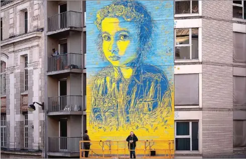  ?? AFP ?? French street artist and painter Christian Guemy (R), known as C215, poses in front of his fresco depicting a Ukrainian young girl with a quote attributed to Ukrainian President Volodymir Zelensky.