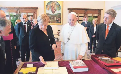  ?? FOTO: AFP ?? Bundeskanz­lerin Angela Merkel – mit Ehemann Joachim Sauer (r.) – und der Papst tauschen im Vatikan Geschenke aus.