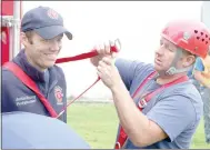  ?? Keith Bryant/The Weekly Vista ?? Firefighte­r-EMT Justin Young holds still while firefighte­r-EMT Josh Whitaker slips a harness on him.